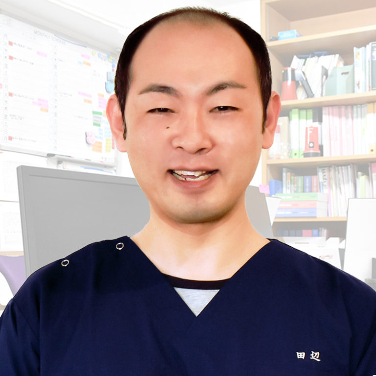 介護施設のスタッフポートレート。紺色のユニフォームを着用し、明るい表情でカメラに向かっている。