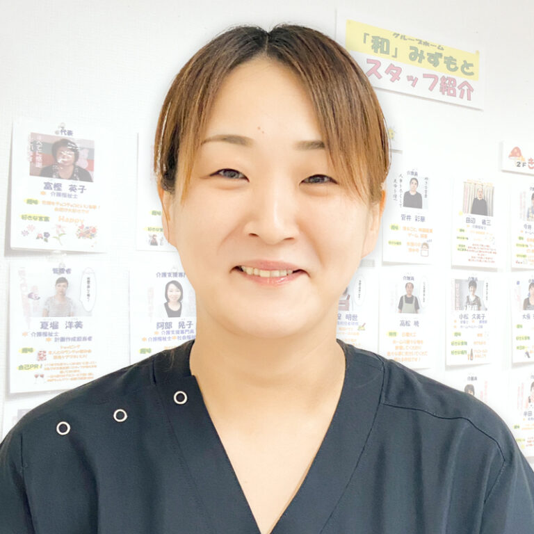 介護施設のスタッフ職員のポートレート写真。背後に職員紹介ボードが見える。